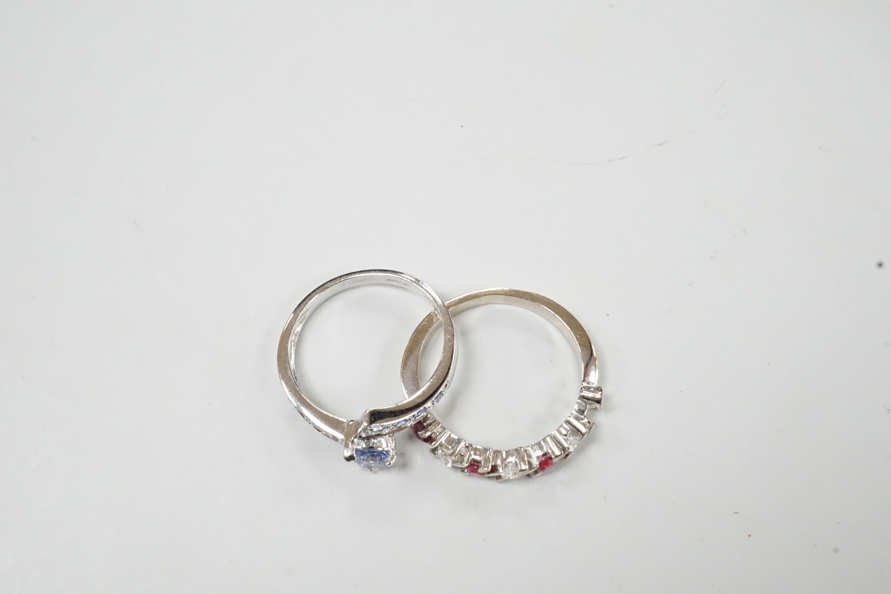 A modern continental white metal ruby and diamond set half hoop ring (ruby missing), size P and and a modern 18ct white gold and blue gem set crossover ring, size N/O, gross weight for both, 7.1 grams.